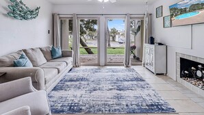 A living room with a beige sofa, a blue patterned rug, a ceiling fan, and a view of a backyard with a pool. - Adventure House Rryc17 2 Bedroom Condo by RedAwning (Rockport)