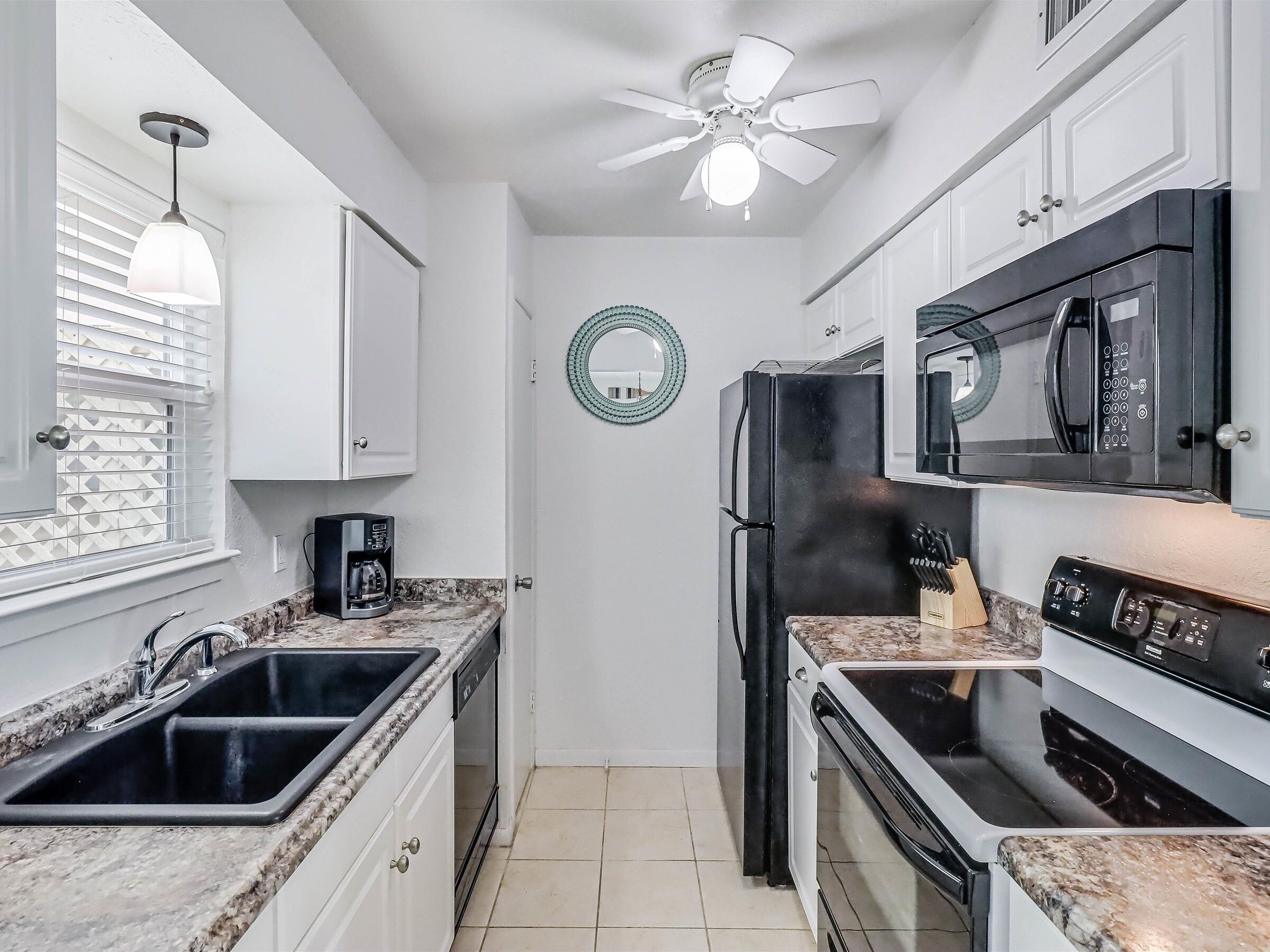 A compact kitchen with white cabinets, a black refrigerator, a microwave, a stove, and a ceiling fan.