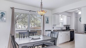 A modern kitchen with white cabinets, a dining table with chairs, and a hanging light fixture. - Adventure House Rryc17 2 Bedroom Condo by RedAwning (Rockport)