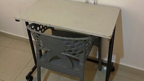 Een klein, opklapbaar tafeltje met een eenvoudig ontwerp, geplaatst tegen een effen muur met een stopcontact.