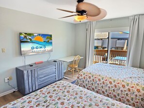 A hotel room with a bed, a desk, a chair, a TV on the wall, and a balcony with a view.