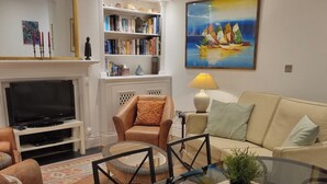 A living room with a glass coffee table, leather sofa, and a bookshelf. - Elegant 2 Bedroom Garden Maisonette near Olympia (London)