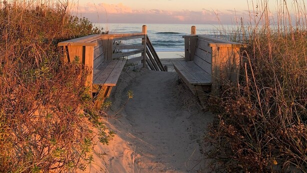 Un sentier en bois mène à une plage, et de chaque côté, une clôture en bois borde le chemin.