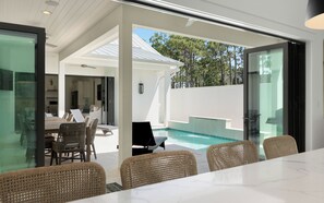 A modern outdoor dining area with wicker chairs and a glass table, overlooking a swimming pool. - Slim Shady + Pool, Golf Cart, Easy Access & Bikes (Santa Rosa Beach)