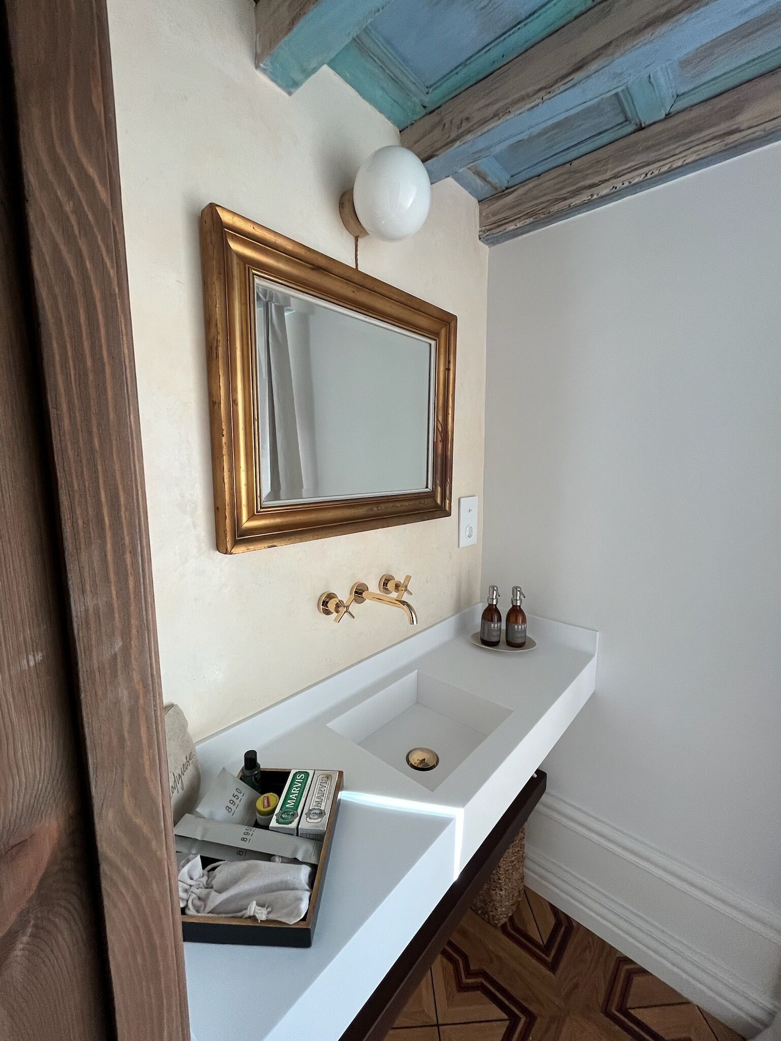 A bathroom with a white sink, a gold-framed mirror, and a white wall.
