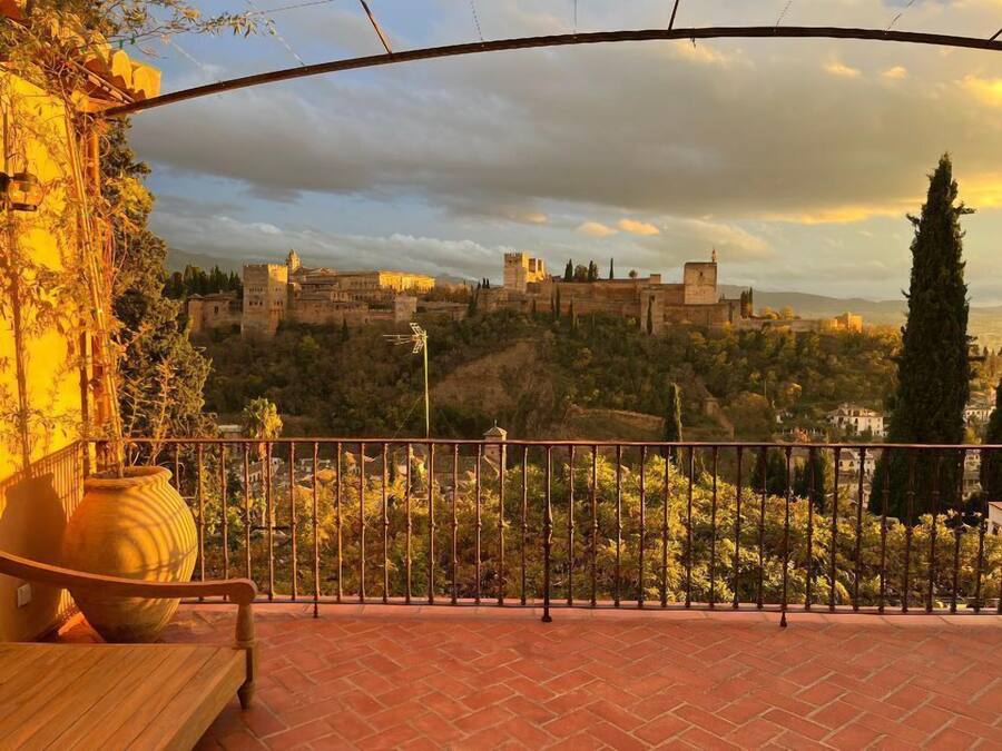 Una terraza con vistas a un castillo histórico en una colina, un banco de madera y una barandilla de metal.