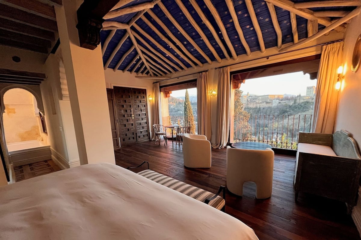 A hotel room with a large bed, a balcony with a view, and a wooden ceiling.
