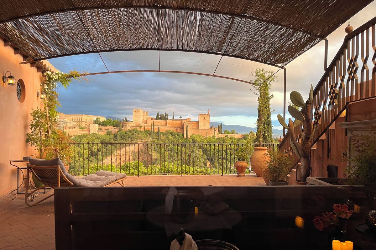 A balcony with a view of a historic city wall, a pergola, and potted plants.