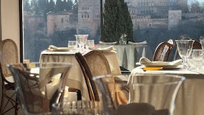 Comedor con mesas dispuestas para una comida, con vistas a un paisaje urbano histórico con edificios antiguos y una torre destacada.