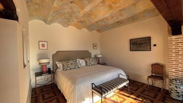 A bedroom with a bed, two bedside tables, a bench, a chair, and a decorative ceiling.