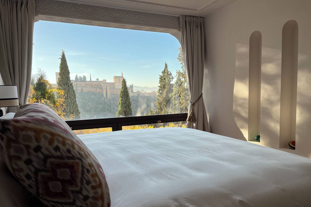 A hotel room with a large bed, a view of a historic building, and a balcony with curtains.