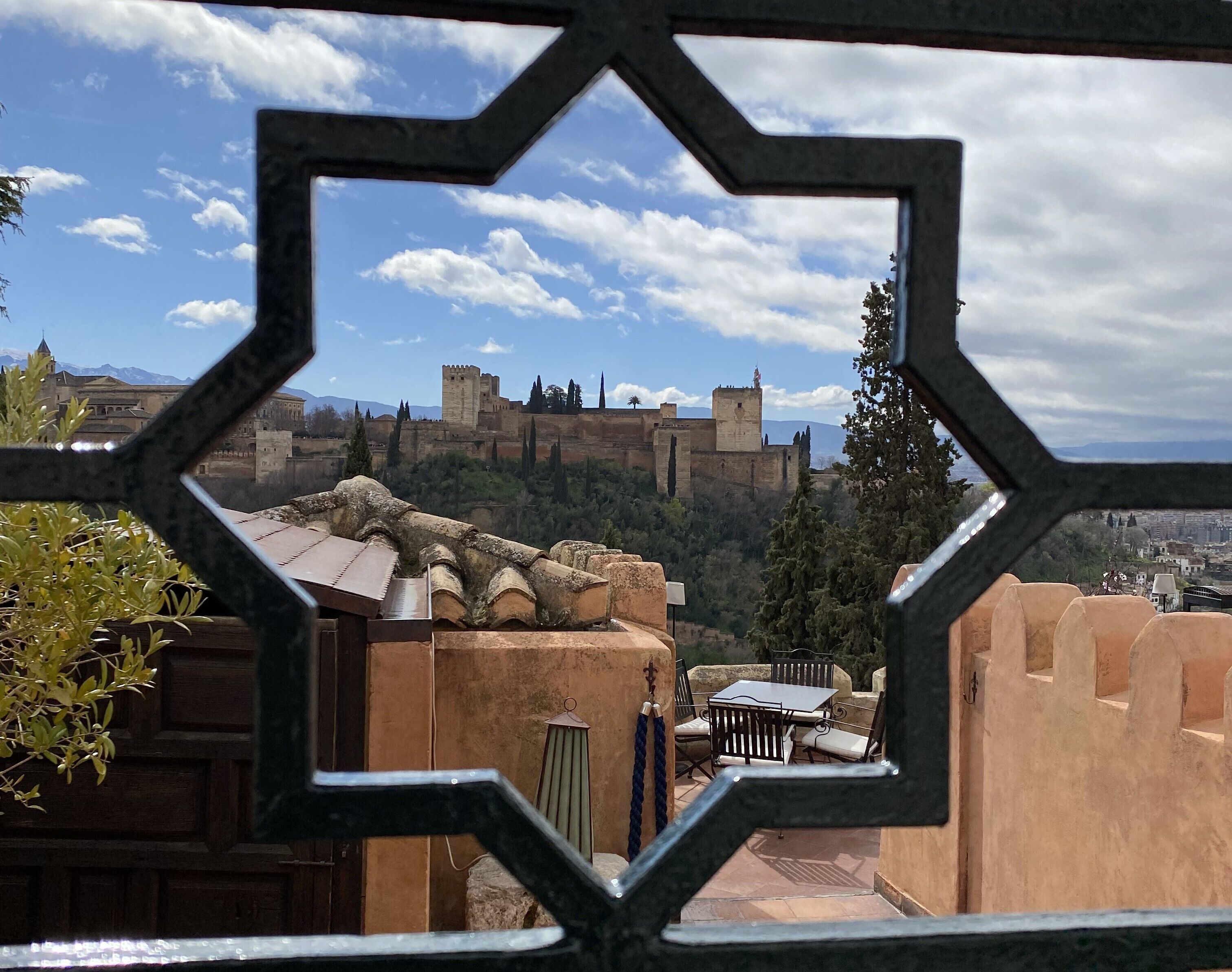 Vista a través de una ventana de diseño geométrico que muestra un castillo en una colina, con un patio al frente.
