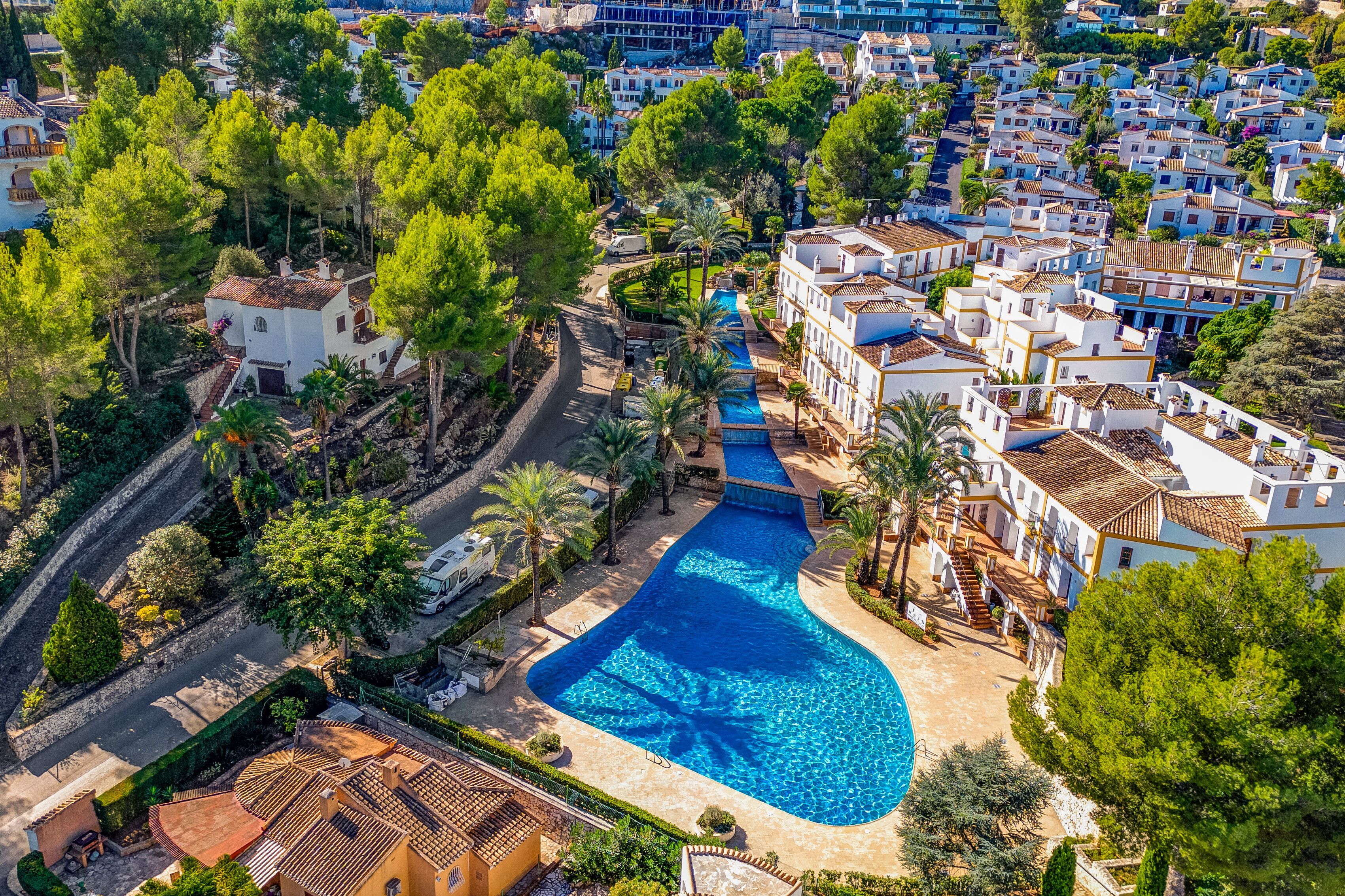 An aerial view of a coastal resort with a large swimming pool, white buildings, and lush greenery.