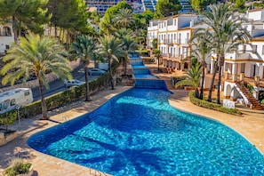 A swimming pool with a clear blue water, surrounded by palm trees and a white building with balconies. - Pool, Sea & Relaxation – Your Holiday Home in La Sella near Dénia (La Sella)