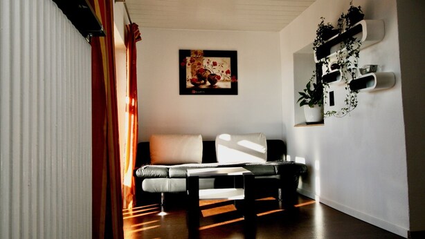 A modern living room with a sofa, a coffee table, and a painting on the wall. - Ferienwohnung in Höhenlage mit Traumausblick (Sankt Oswald-Riedlhütte)