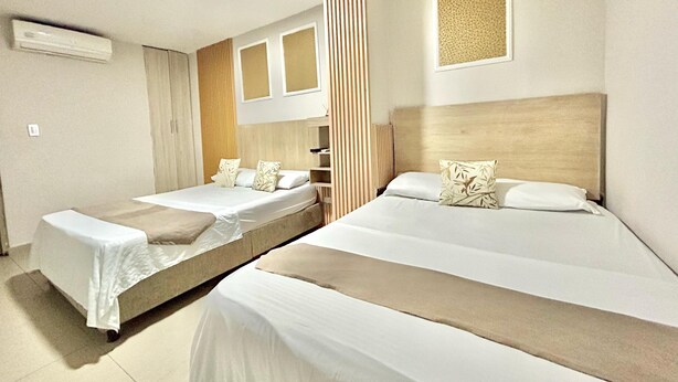 A hotel room with two beds, a window with blinds, a radiator, and an air conditioning unit.