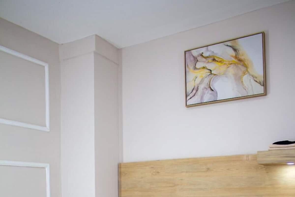 Ein ordentlich bezogenes Bett mit weißen Leinen, einem Holzkopfteil und einem an der Wand hängenden abstrakten Gemälde.