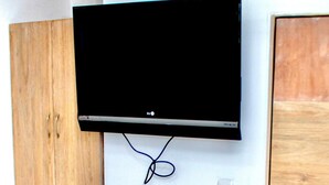 A flat-screen TV mounted on a white wall, with a wooden cabinet to the left and an air conditioning unit above.