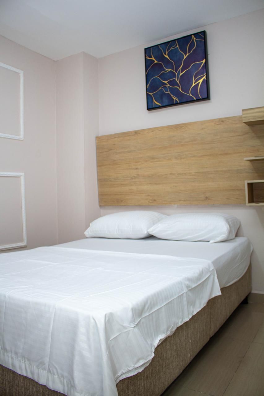 A neatly made bed with white linens in a room with light-colored walls and a wooden headboard.