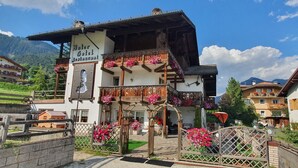 Un hotel de estilo alpino tradicional con un balcón decorado con flores, un letrero que indica que es restaurante, y vistas del paisaje montañoso circundante.
