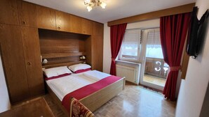 Un dormitorio con cabecera de madera, cama con ropa de cama blanca y roja, ventana con cortinas rojas y un radiador.