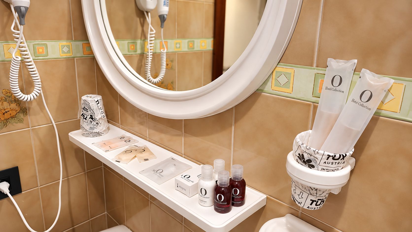 A bathroom with a mirror, a towel rack, a shelf with toiletries, and a wall-mounted phone.