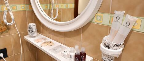 A bathroom with a mirror, a towel rack, a shelf with toiletries, and a wall-mounted phone.