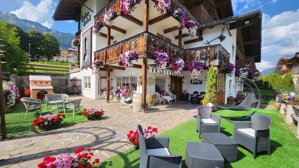 Una cabaña tradicional con mobiliario exterior, un patio de piedra y cestas de flores colgantes.