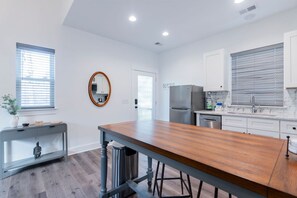 A modern kitchen with white cabinets, a stainless steel refrigerator, and a wooden dining table.