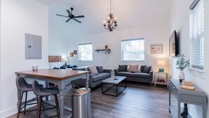 A spacious living room with a dining area, a ceiling fan, a chandelier, and large windows. - Old Town Loft, a delightful vacation rental in the heart of historic Bluffton (Bluffton)