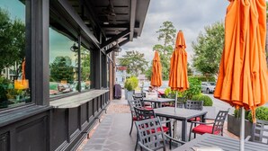 An outdoor seating area with tables and chairs, orange umbrellas, and a view of the street. - Old Town Loft, a delightful vacation rental in the heart of historic Bluffton (Bluffton)