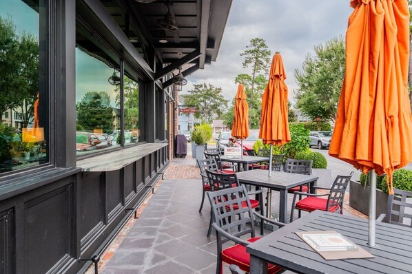 An outdoor seating area with tables and chairs, orange umbrellas, and a view of the street.
