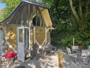 Eine Holzhütte mit geneigtem Dach, einer Tür und einer kleinen Veranda mit Stühlen und einem Tisch.
