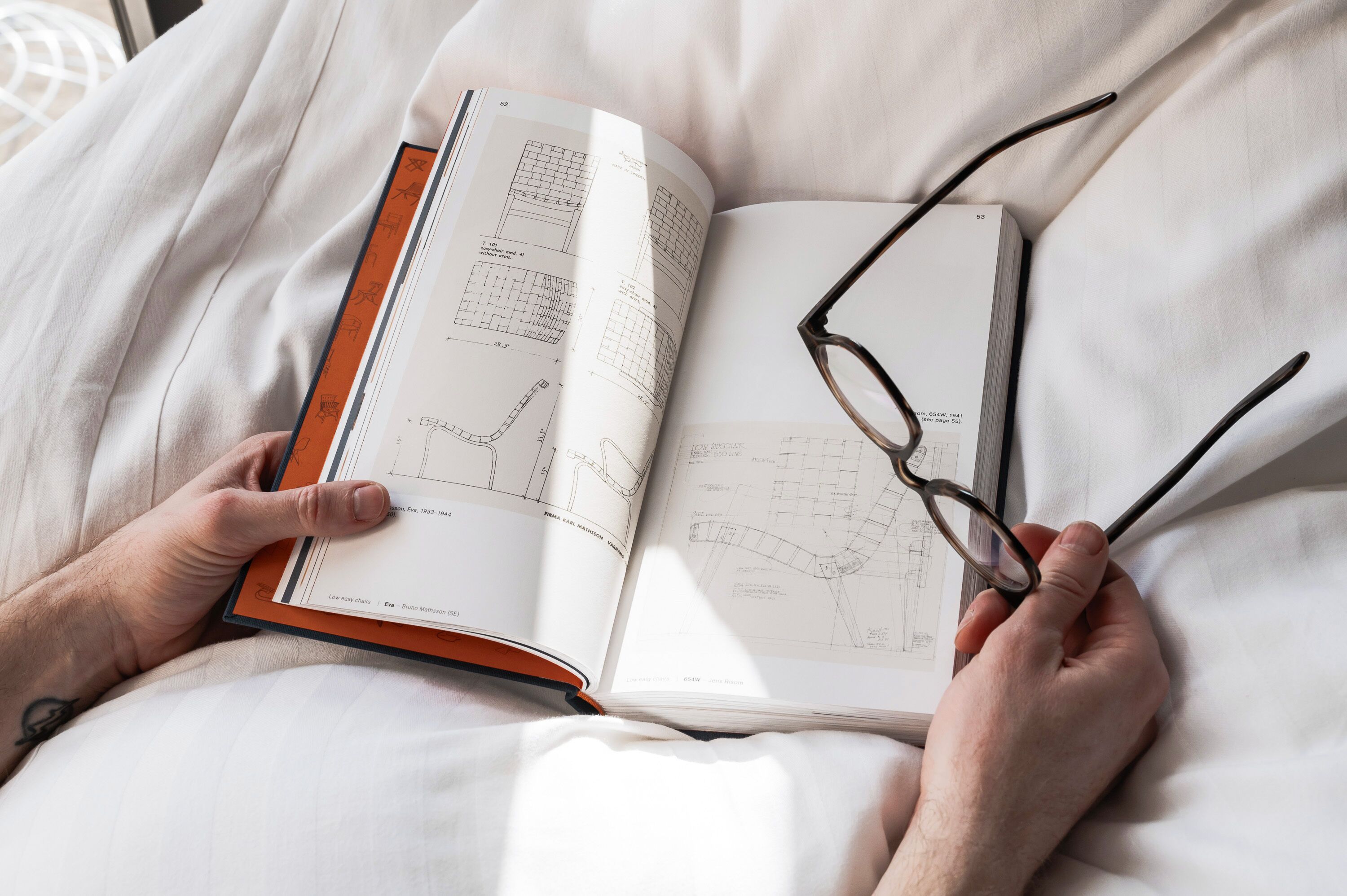 Una persona leyendo un libro con planos arquitectónicos sobre una cama.