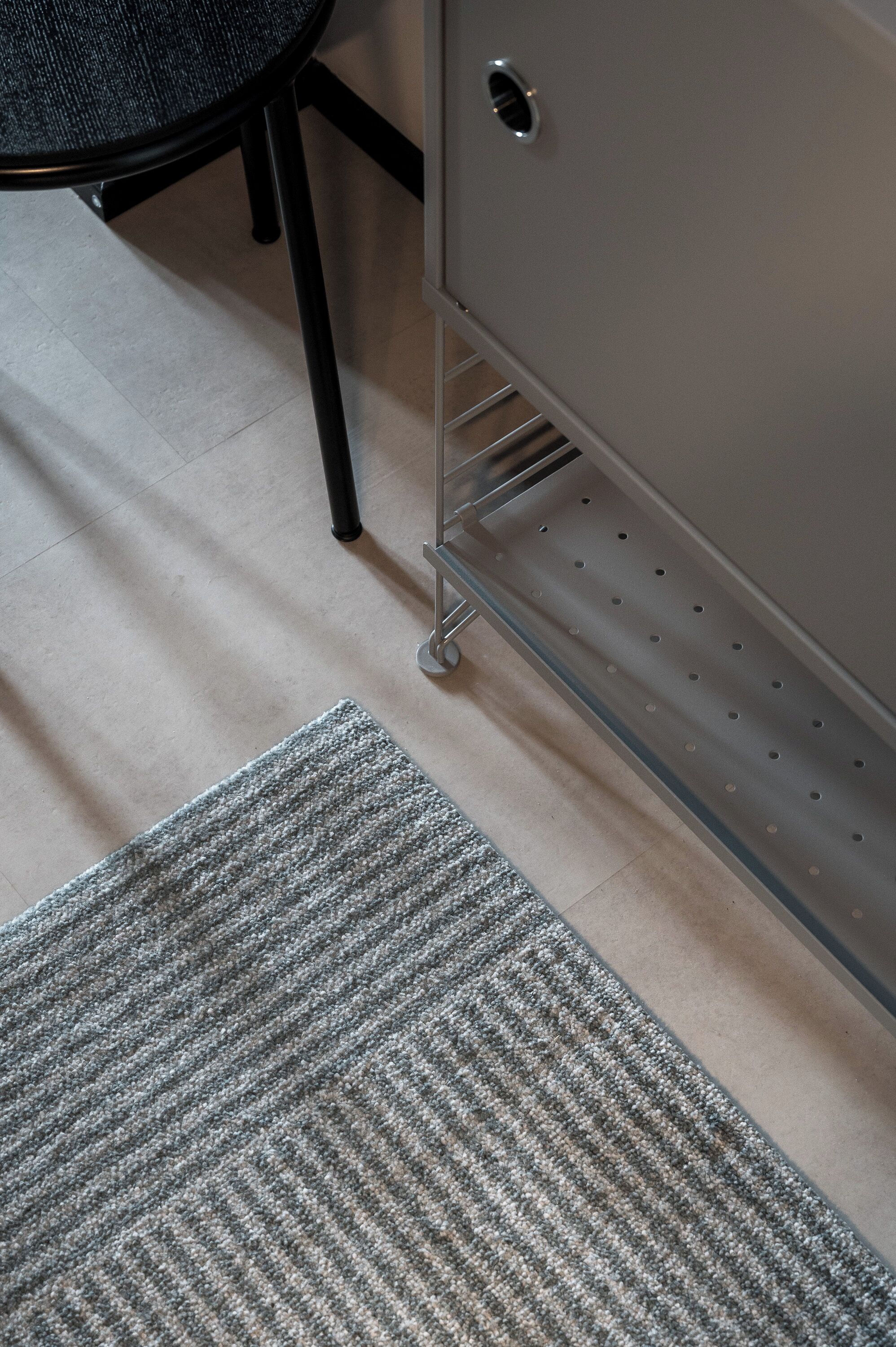 A portion of a room with a grey carpet, a metal filing cabinet, and a chair with a dark seat.