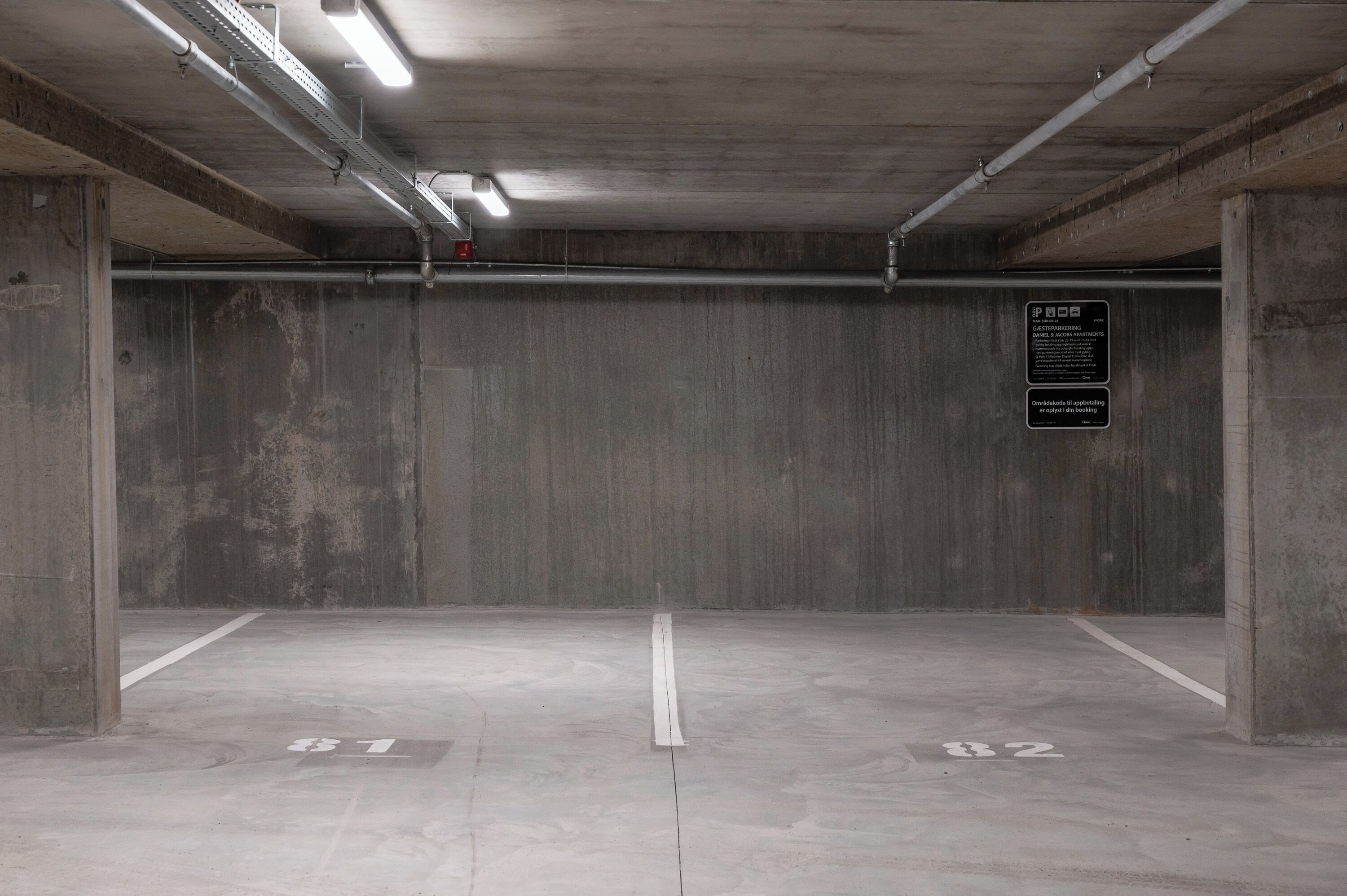 An empty parking garage with concrete walls, a flat floor, and overhead fluorescent lighting.