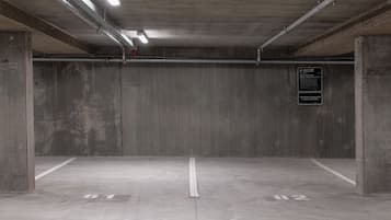 An empty parking garage with concrete walls, a flat floor, and overhead fluorescent lighting.