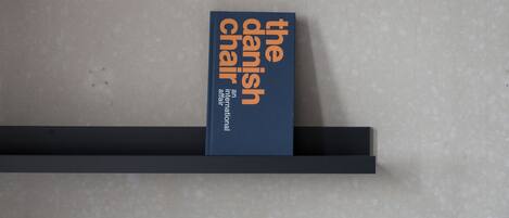 Een boek met de titel 'The Danish Chair' op een plank tegen een effen muur.
