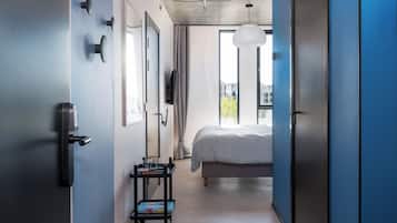 Une chambre d’hôtel moderne avec un grand lit, une télévision et un petit chariot sur lequel se trouve un magazine.