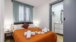 A hotel room with a bed, a nightstand, a bedside table, a window with curtains, a bathroom with a mirror, and a door. - Alojamiento Sierra Nevada Viva.  (Otura)