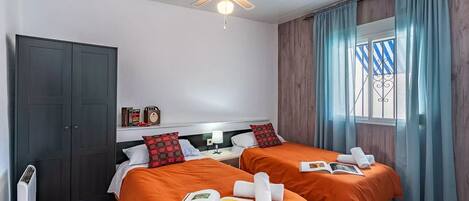 A hotel room with two beds, a ceiling fan, a window with curtains, and a radiator.