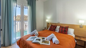 A hotel room with a large bed, two bedside lamps, a wooden headboard, and a view of a balcony with a railing. - Alojamiento Sierra Nevada Viva.  (Otura)