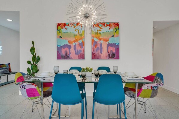 A dining area with a glass table, blue chairs, and colorful artwork on the wall.