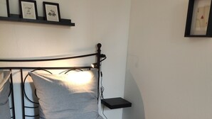 En pænt redt seng med sengegavl, et natbord og en vægmonteret hylde med billeder i rammer.
