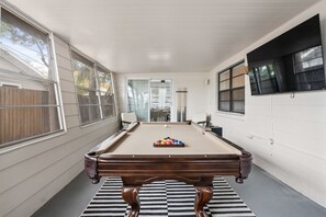 A pool table in a room with white walls, large windows, and a striped rug.