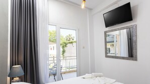 Habitación de hotel con cama, televisor en la pared, espejo, lámpara y vistas al balcón exterior.