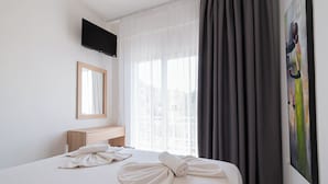 Una habitación de hotel con cama, mesita de noche, televisor montado en la pared y ventana con cortinas.