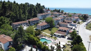 Vista aérea de una zona residencial costera con varios edificios de dos pisos, una piscina y una vista despejada del mar.