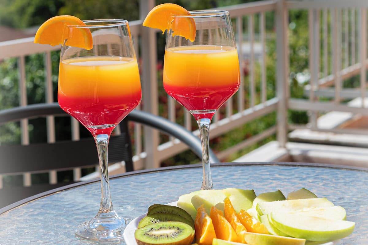 Two glasses of juice with fruit slices on a table outdoors.