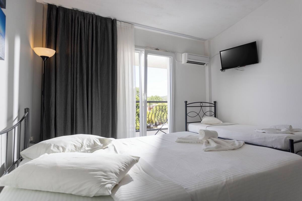 A hotel room with a large bed, a smaller bed, a TV mounted on the wall, and a balcony with a view.